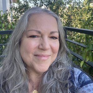 Smiling woman with long gray hair outdoors on a sunny day.